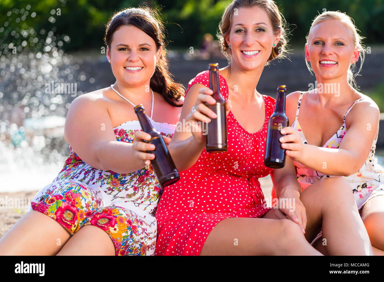 Les amis de boire une bière à river beach Banque D'Images
