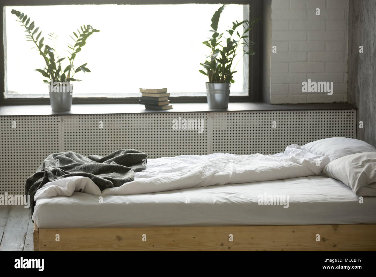 Unmade bed double malpropre pour deux avec literie linge froissé feuille près de fenêtre dans une chambre moderne et confortable design intérieur gris avec personne, vide co Banque D'Images