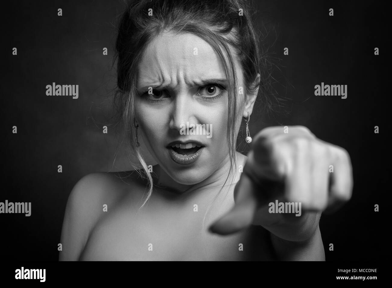 Jeune femme en colère sur fond noir point sur appareil photo, monochrome Banque D'Images