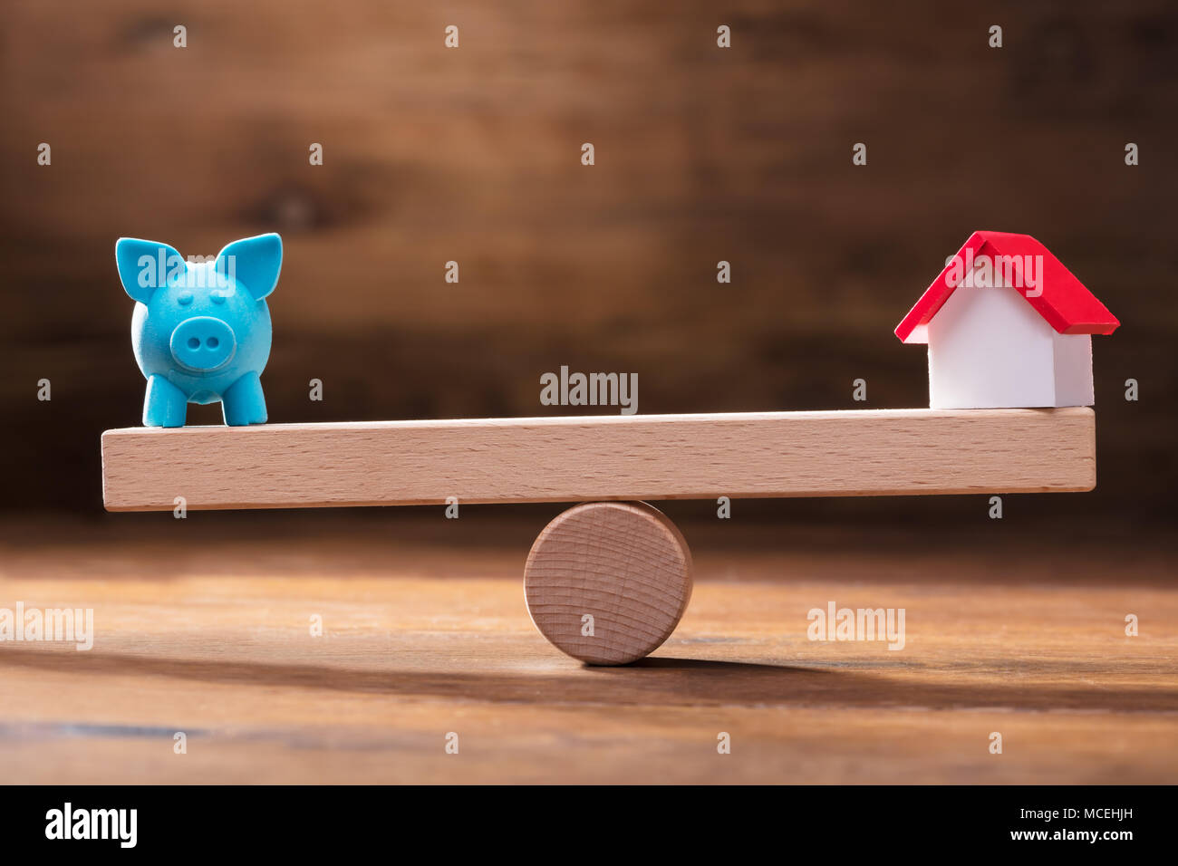 L'équilibre de bleu Piggybank and Miniature House Modèle sur la balançoire en bois Banque D'Images