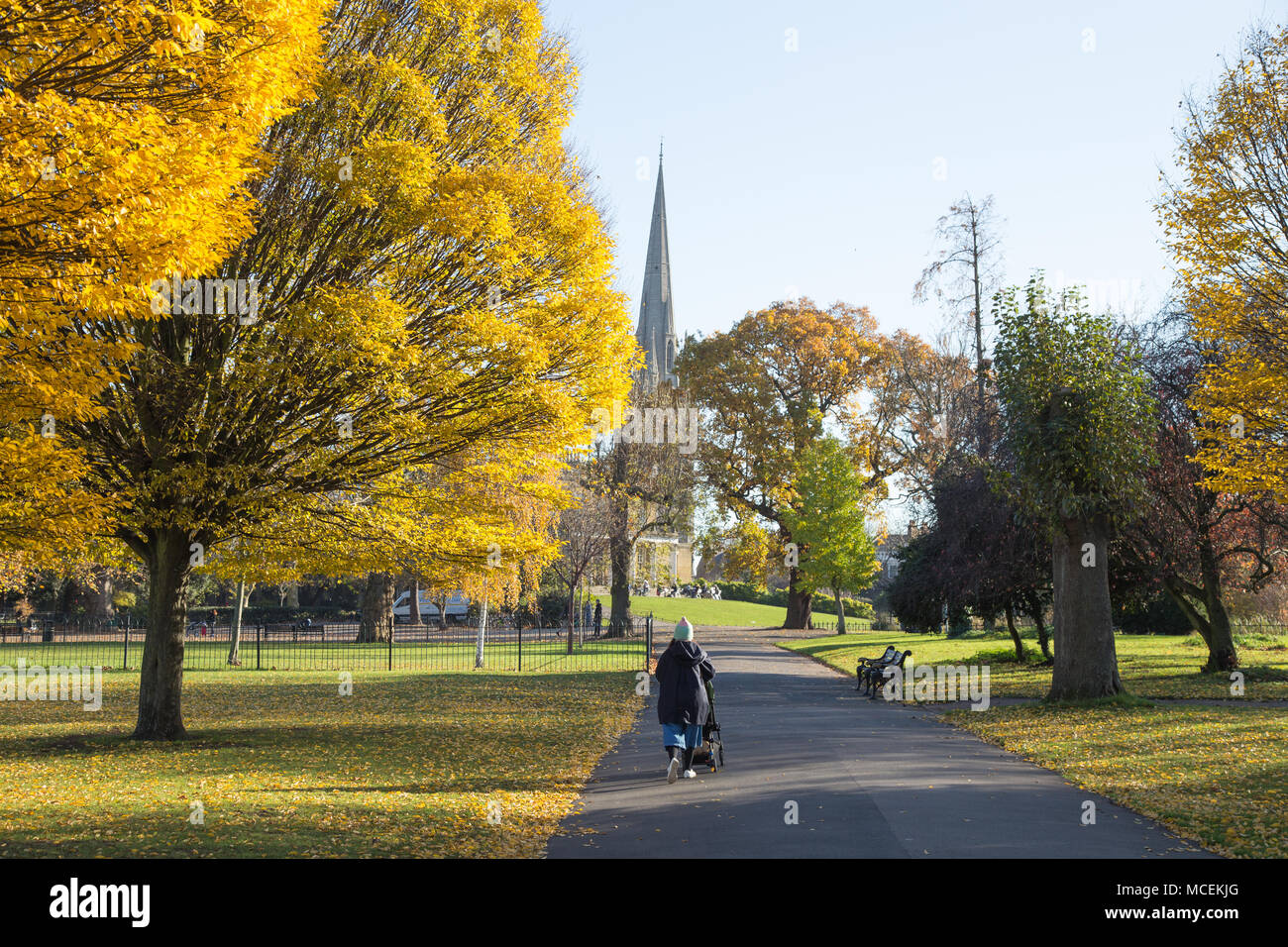 Une mère marchant avec une poussette dans le parc Clissold, Stoke Newington, Londres, au milieu d'arbres aux couleurs automnales dorées avec l'église St Mary en arrière-plan Banque D'Images