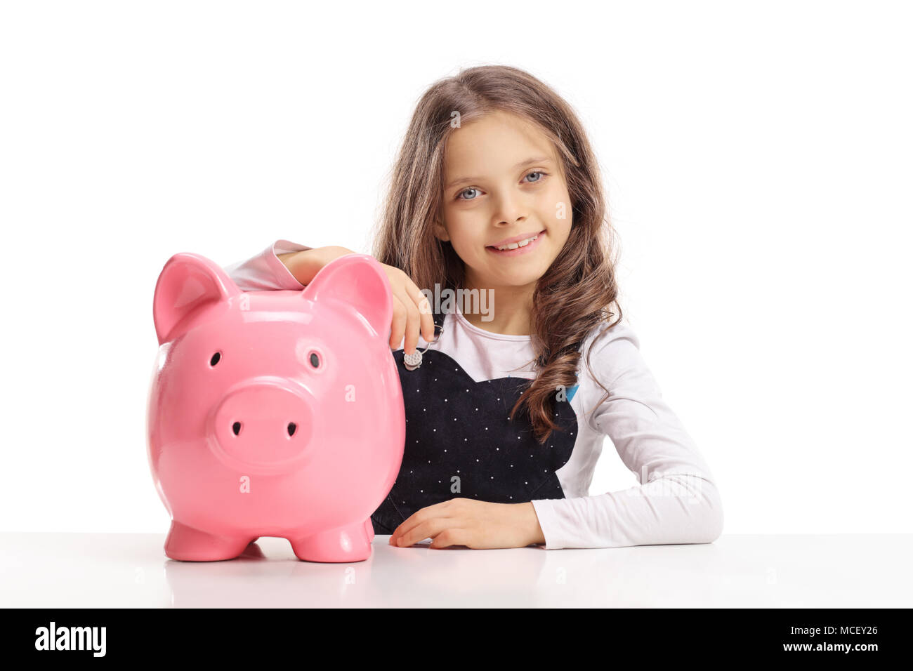 Petite fille avec une tirelire assis à une table isolé sur fond blanc Banque D'Images