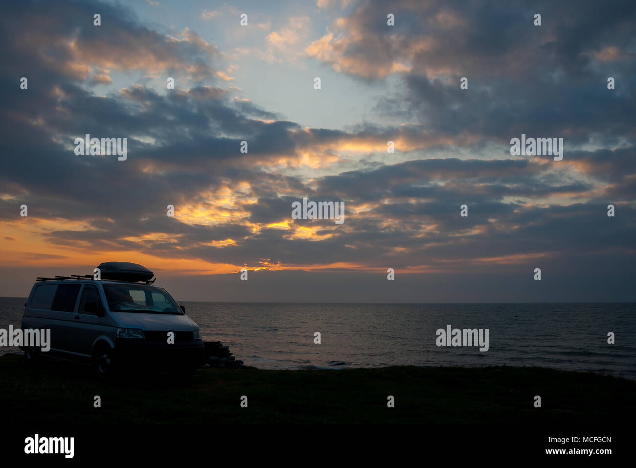 Vue pittoresque du campervan VW transporter argenté garé sur le côté de la falaise surplombant la mer calme au coucher du soleil. Scène spectaculaire du ciel. Staycation Royaume-Uni. Banque D'Images