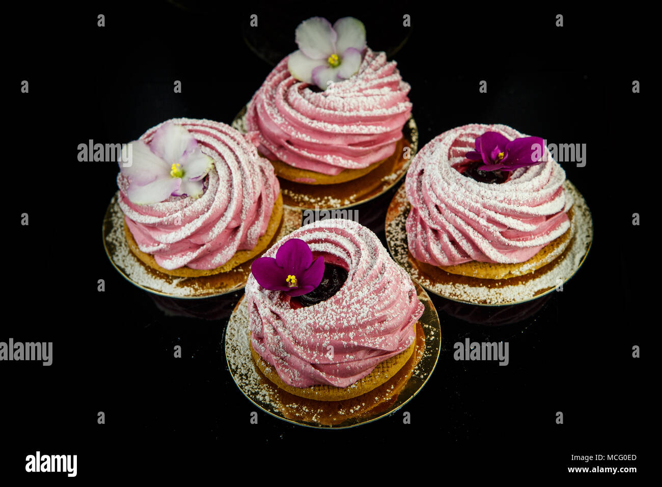 Vue de dessus sur quatre cookies zephyr rose décorée de fleurs violet et blanc sur fond noir miroir d'en haut Banque D'Images
