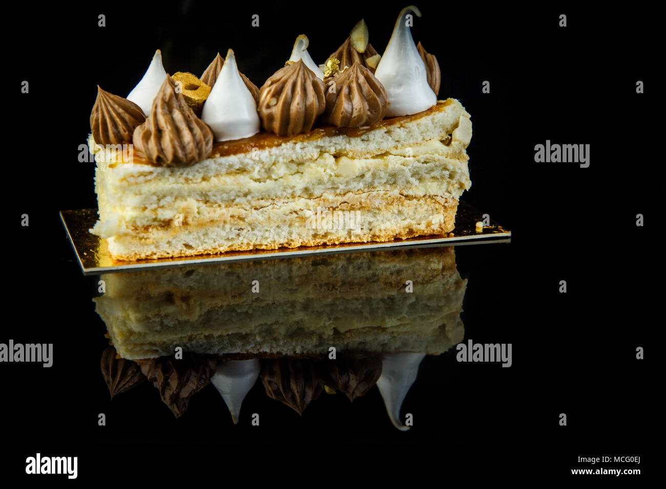 Morceau de gâteau Kiev double couche très décoré de crème au chocolat et noix gros plan sur fond noir avec reflet miroir Banque D'Images