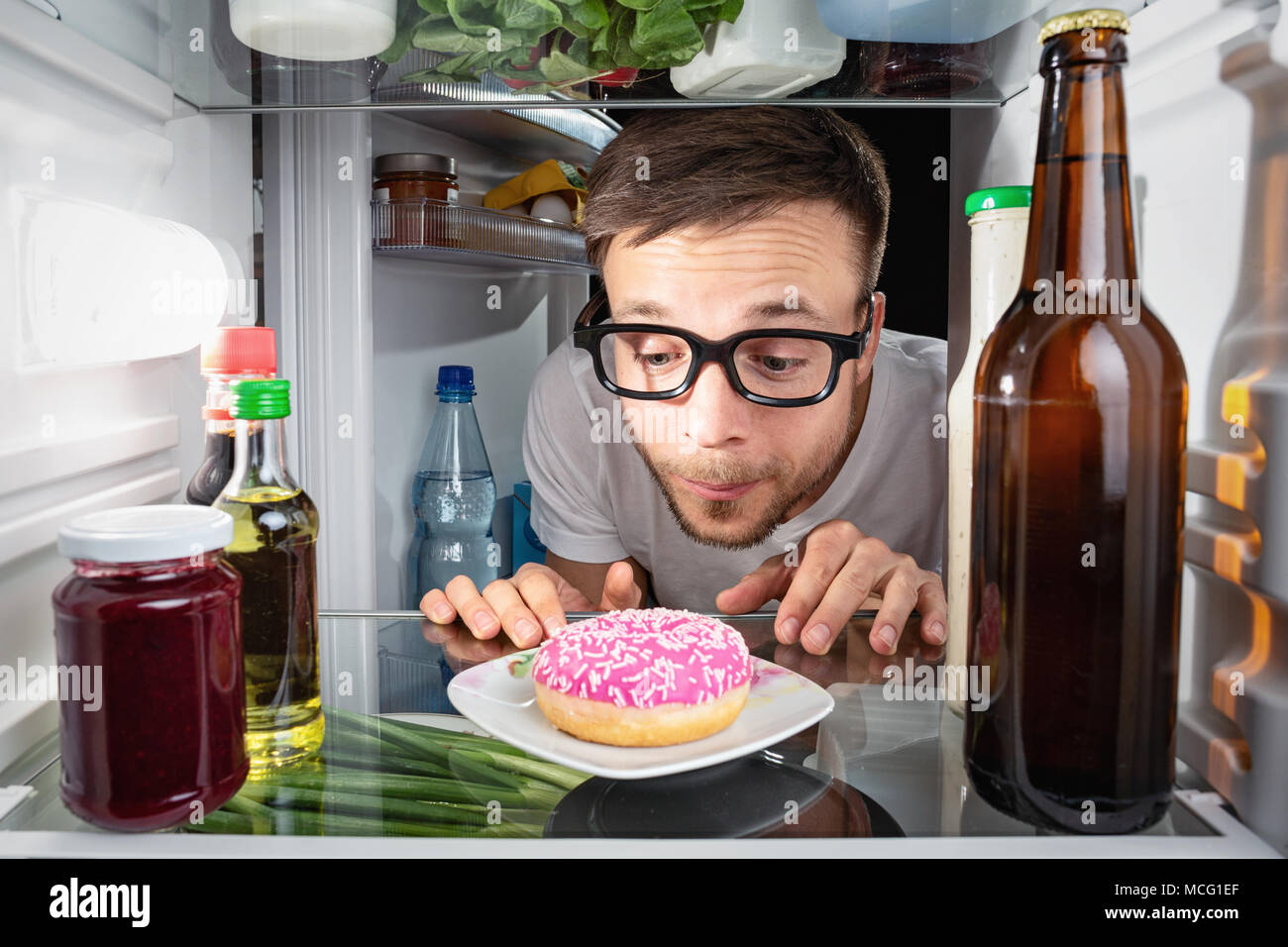 L'homme regardant un donut dans le réfrigérateur Banque D'Images