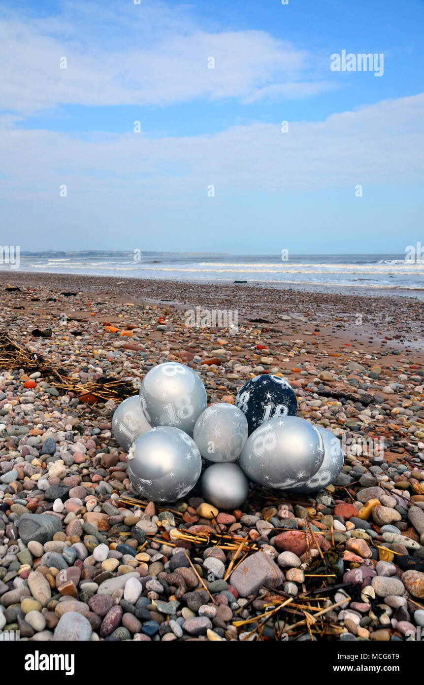 Un faisceau de 18e anniversaire ballons à gaz Hélium qui ont débarqué comme déchets sur une plage. Banque D'Images