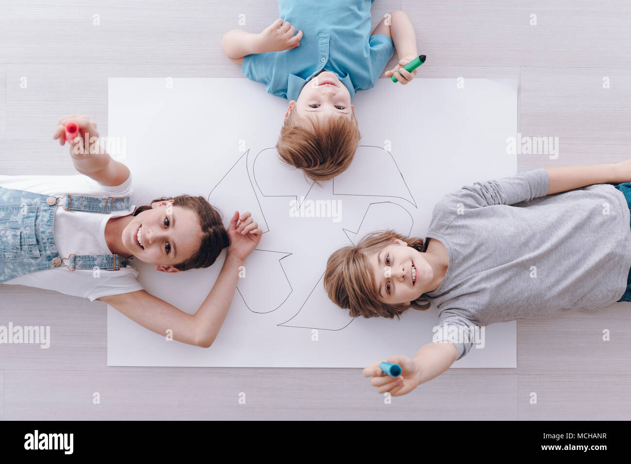 High angle de groupe d'enfants souriants se trouvant sur l'affiche avec signe de recyclage Banque D'Images