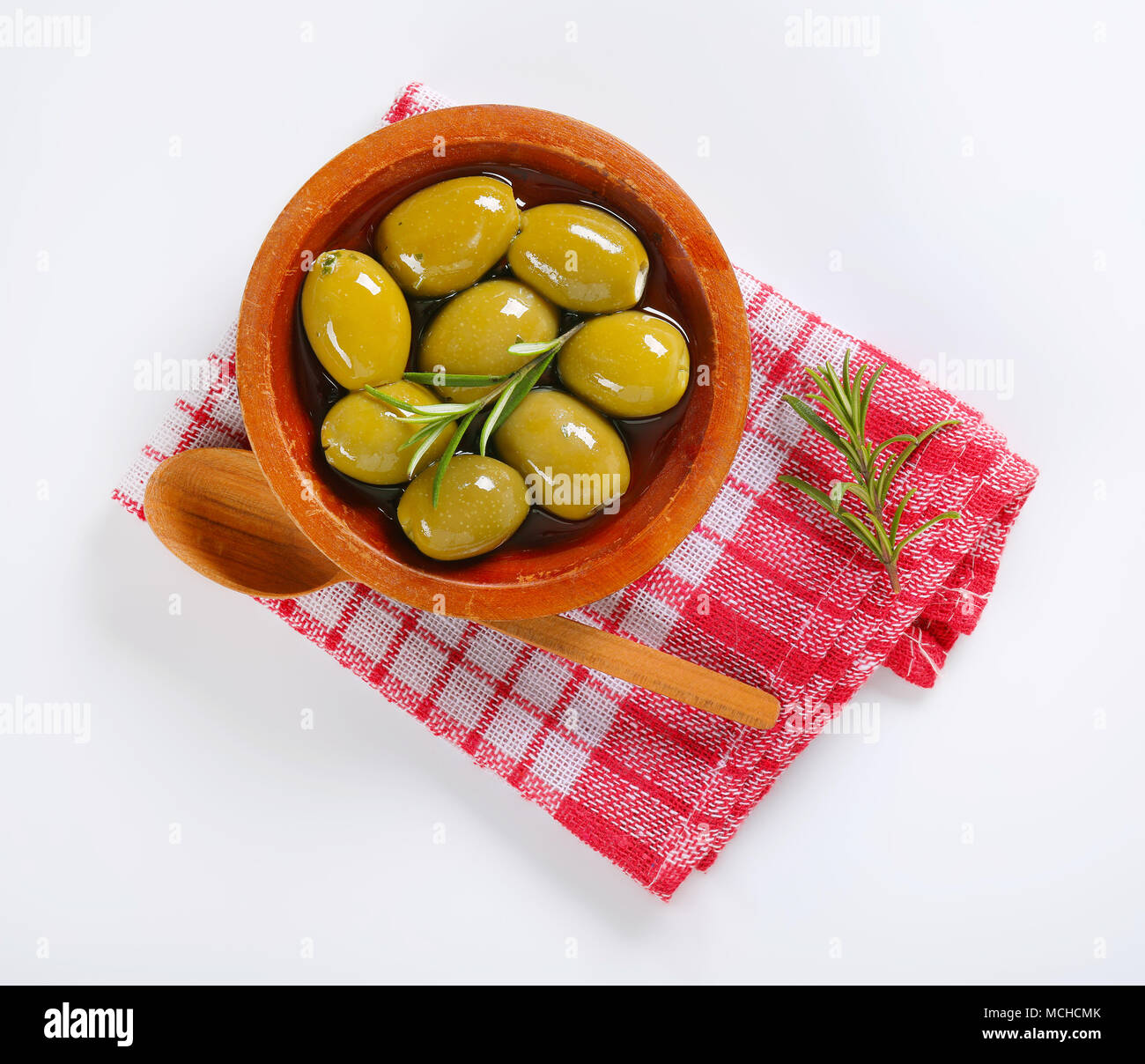 Bol d'olives vertes avec le romarin et cuillère en bois sur le torchon à carreaux Banque D'Images Bol d'olives vertes avec le romarin et cuillère en bois sur le torchon à carreaux Banque D'Images