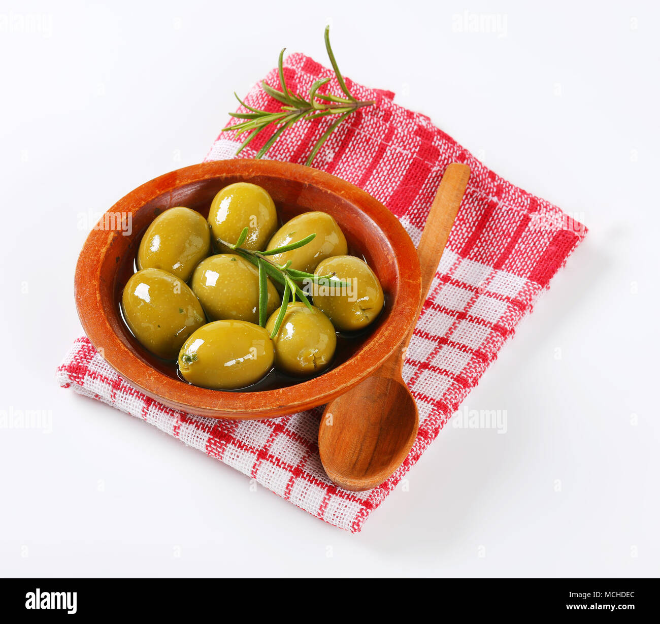 Bol d'olives vertes avec le romarin et cuillère en bois sur le torchon à carreaux Banque D'Images Bol d'olives vertes avec le romarin et cuillère en bois sur le torchon à carreaux Banque D'Images
