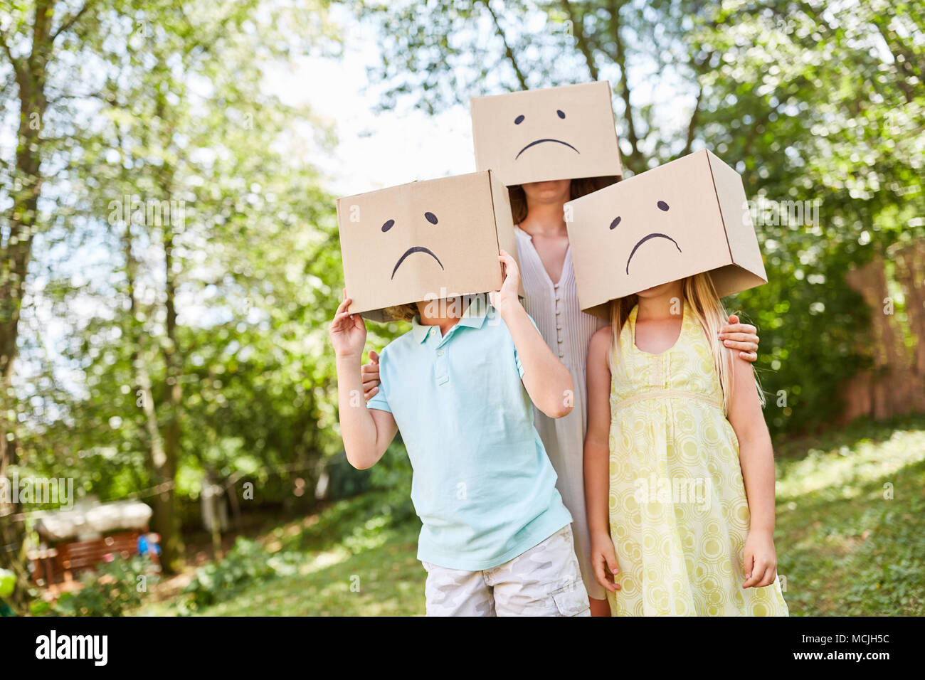 Famille avec des cartons sur la tête l'air triste dans le jardin en été Banque D'Images