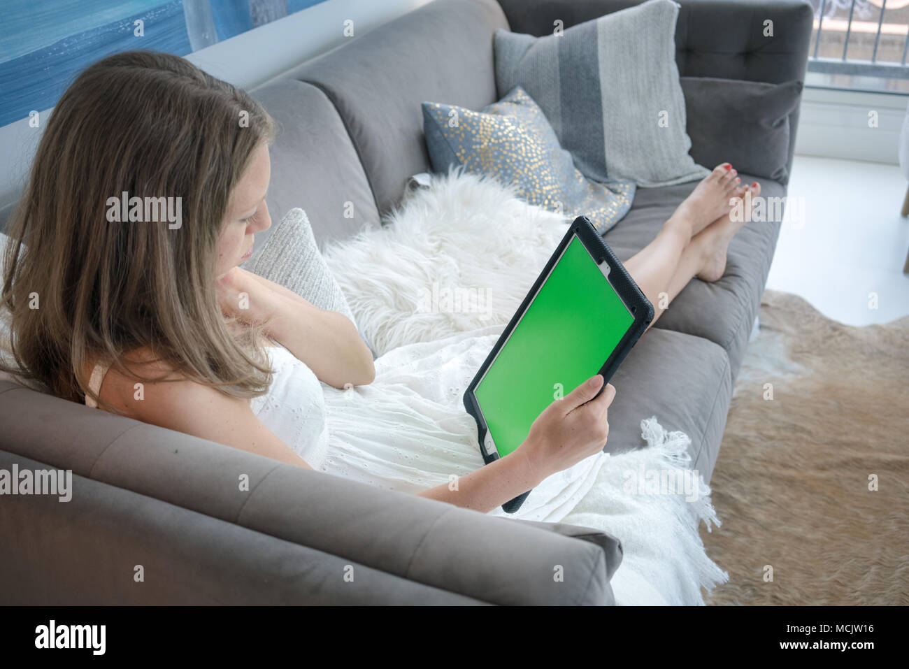 Young woman using digital tablet on sofa in living room Banque D'Images