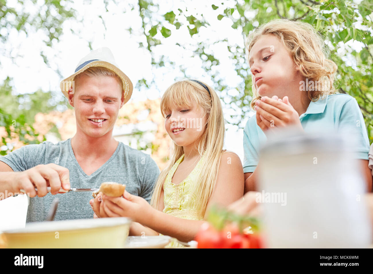 Coups de père du beurre sur une baguette tout en prenant le petit déjeuner avec les enfants dans le jardin Banque D'Images