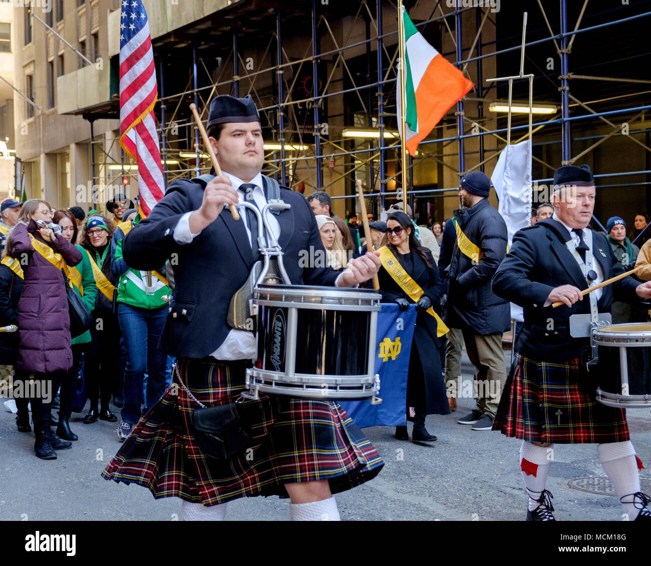 Les hommes en kilts mars & jouer de la batterie. American Celtic Pipe Band, New York City Saint Patrick's Day Parade, 2018. Les gens derrière avec American & drapeaux irlandais. Banque D'Images