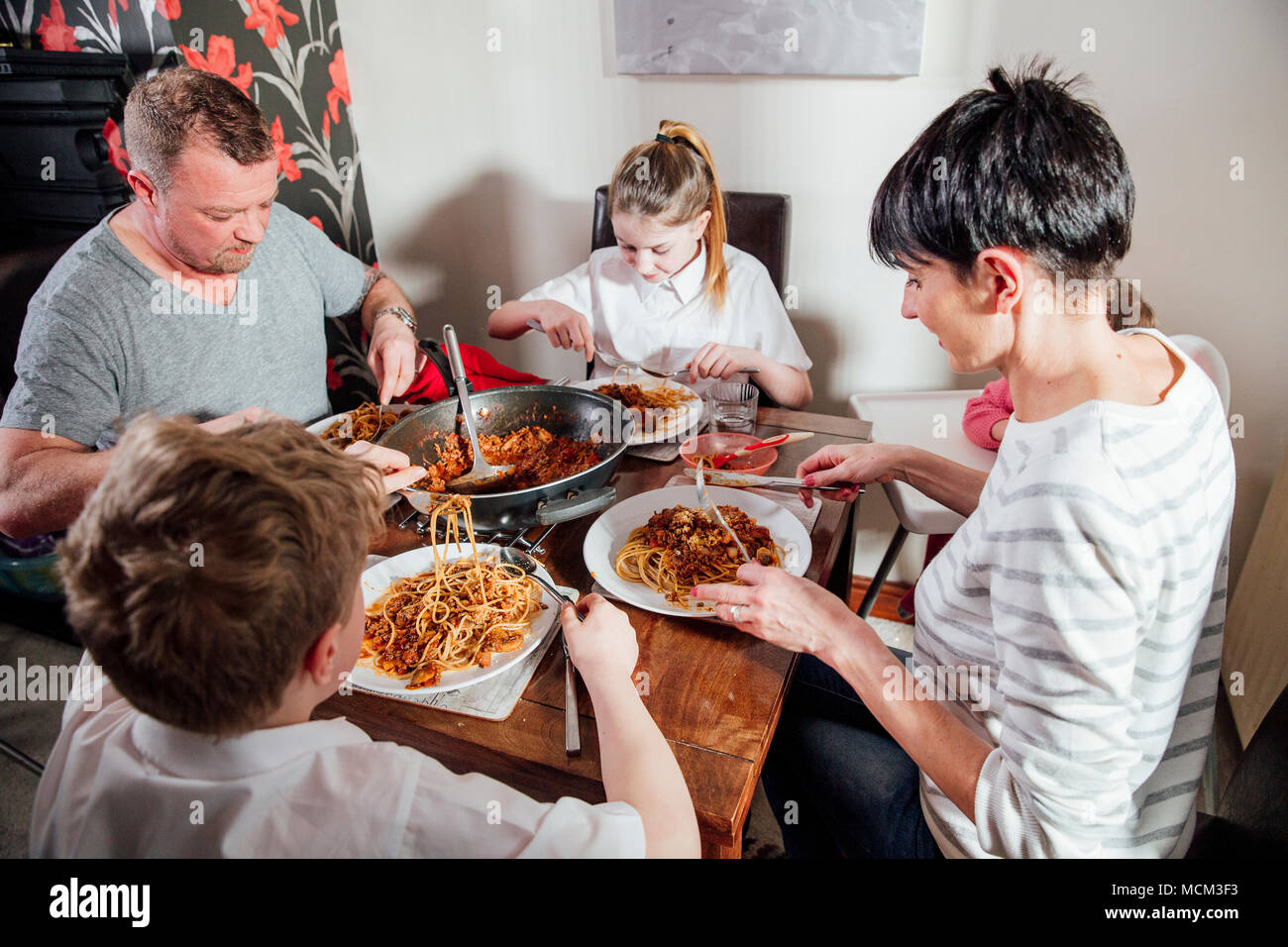 La famille bénéficiant d'un spaghetti bolognese ensemble à la maison. Ils sont assis à la table à manger avec la fille de bébé dans un siège bébé. Banque D'Images