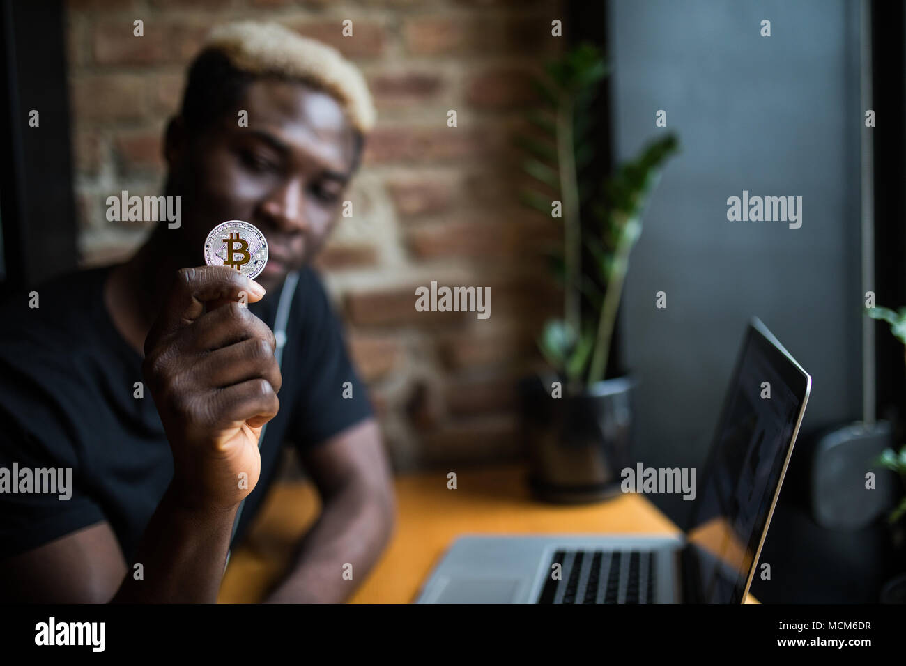 Homme jeune avec en main des bitcoins en face de l'ordinateur portable Banque D'Images