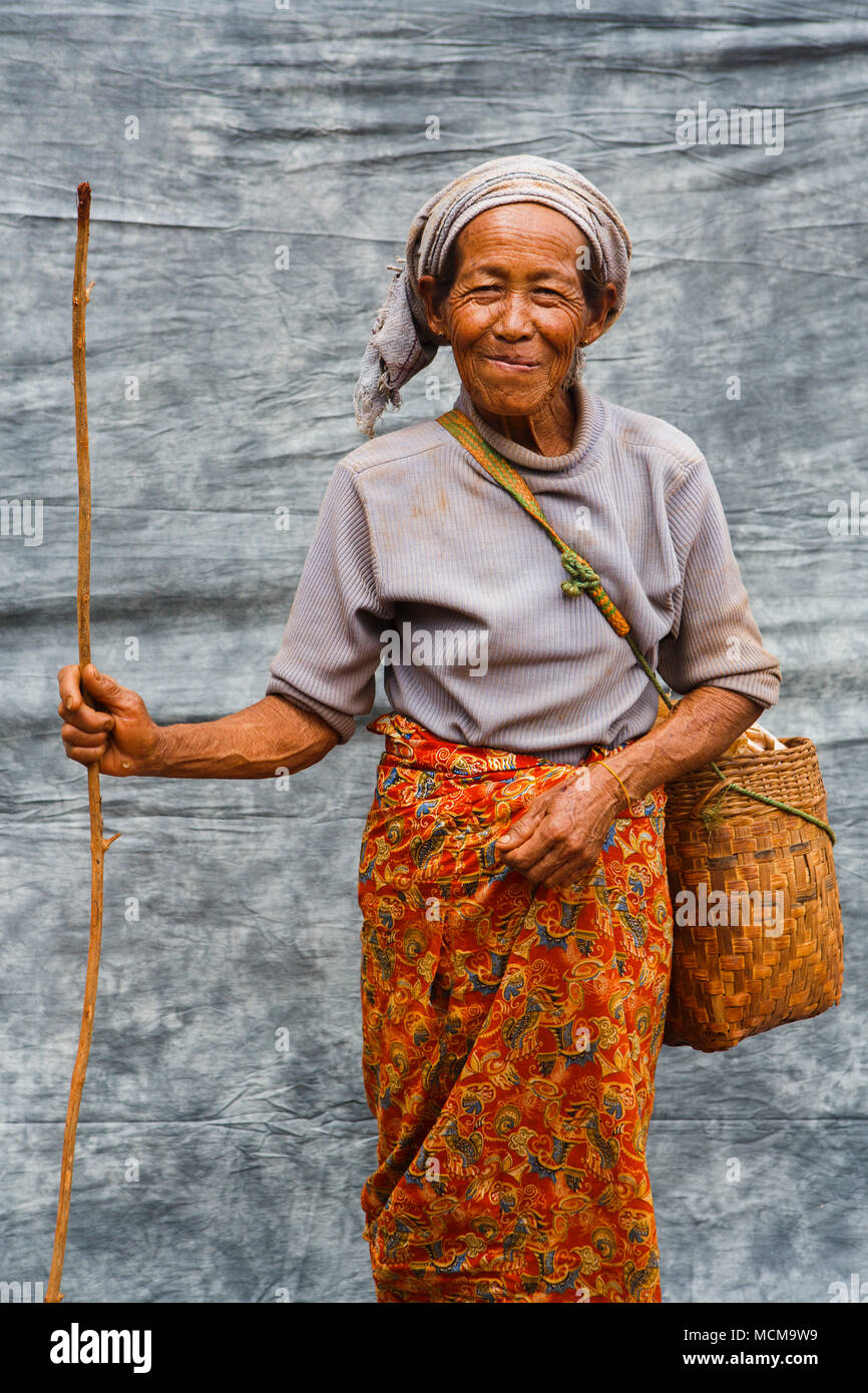 Portrait of senior female farmer posing avec sac et de brindilles en face de tissu gris, l'État de Shan, Myanmar Banque D'Images