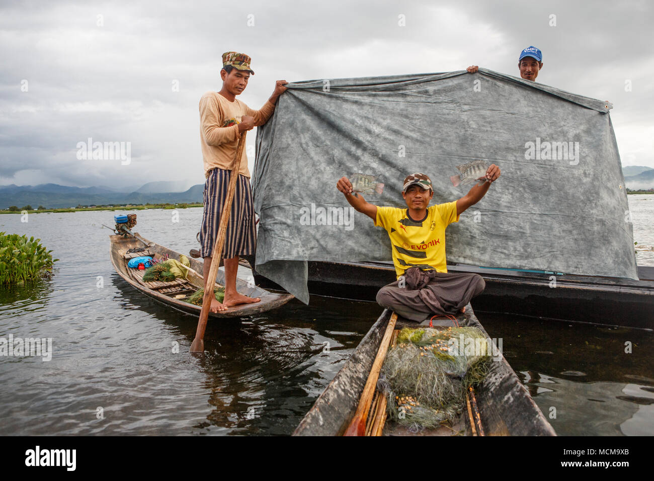 Posant en bateau Pêcheur de poissons avec tissu gris contre tenu par deux amis, l'État de Shan, Myanmar Banque D'Images