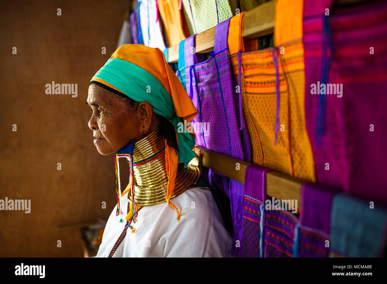 Portrait of senior woman wearing colliers traditionnels debout à côté des vêtements colorés accroché sur des poutres en bois, l'État de Shan, Myanmar Banque D'Images