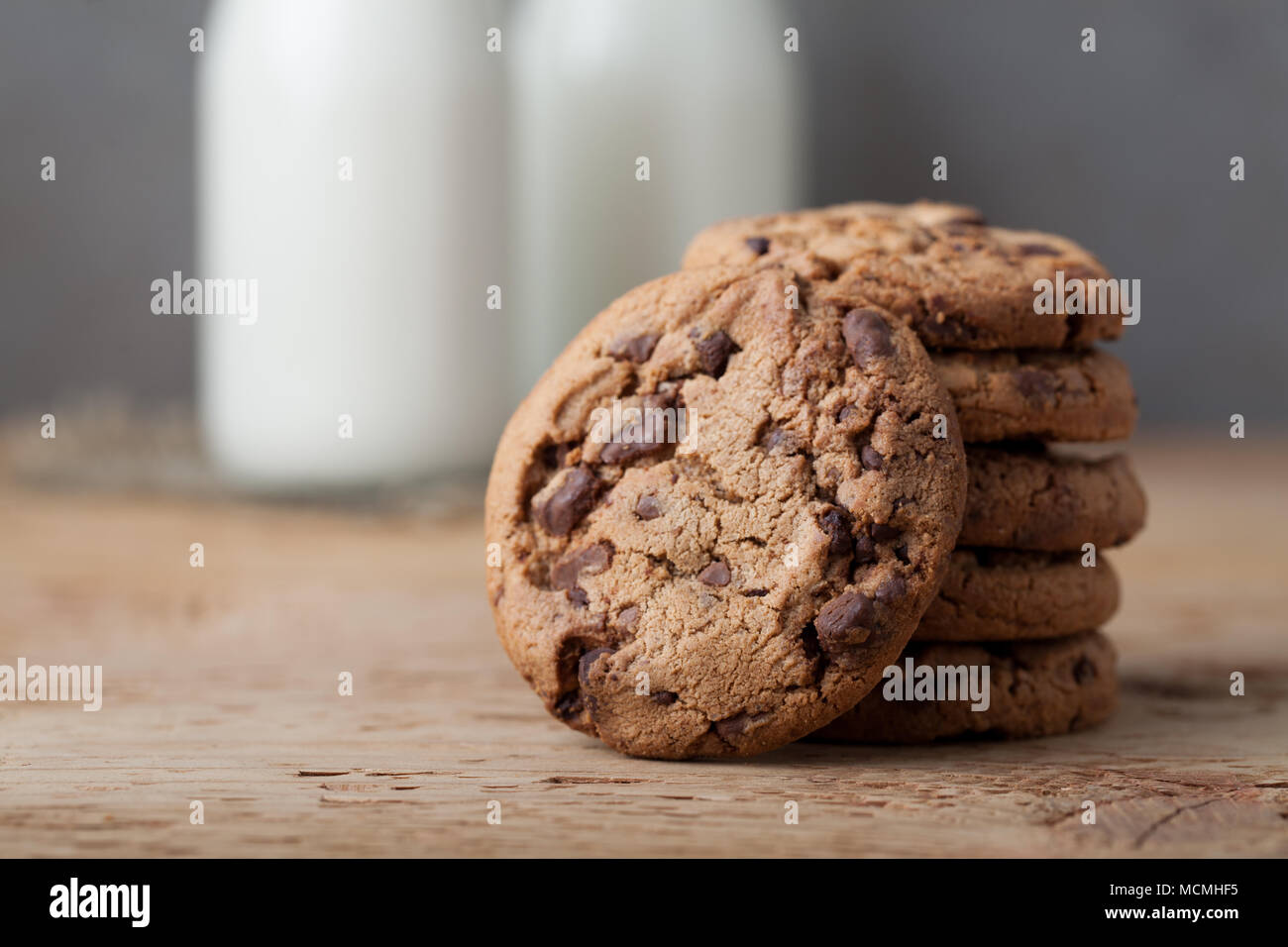 Une pile de cookies au chocolat au lait et de deux bouteilles de lait sur une table en bois. Banque D'Images