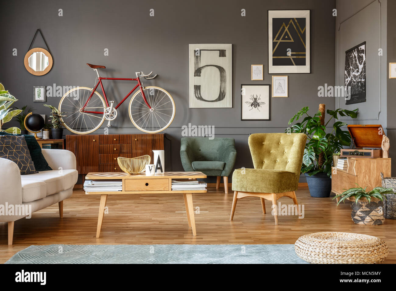 Collection d'art sur un mur gris, table basse en bois, fauteuil et du vélo dans un salon intérieur Banque D'Images