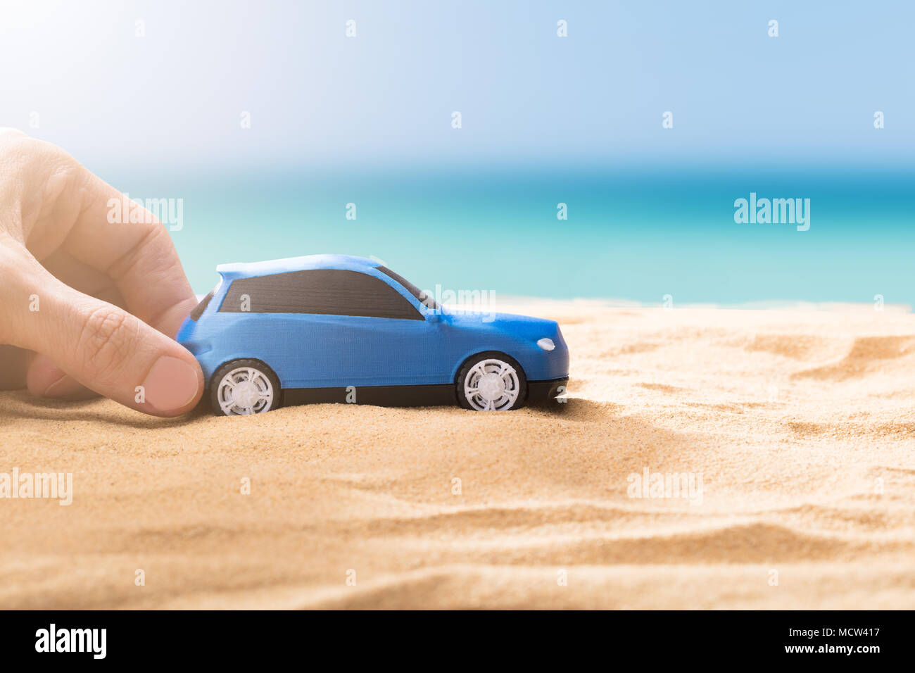 Human Hand Holding petite voiture bleue On Sandy Beach Banque D'Images