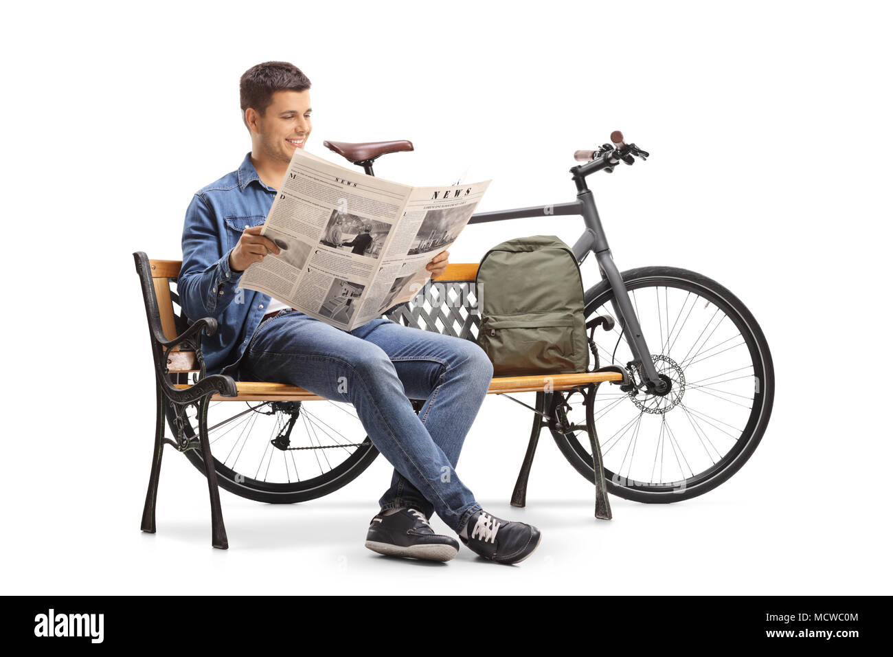 Jeune mec avec un vélo et un sac à dos, assis sur un banc en bois et lire un journal isolé sur fond blanc Banque D'Images