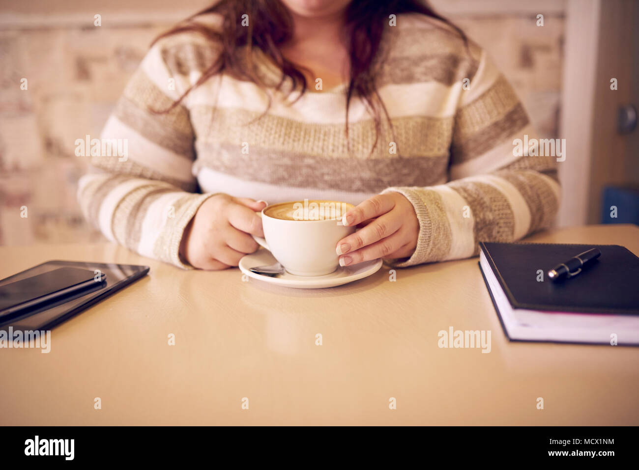 Culture sans tête d'un overwight légèrement woman sitting at a cafe table avec son carnet de notes et d'un comprimé à l'autre de son, et une nouvelle tasse de café chaud Banque D'Images