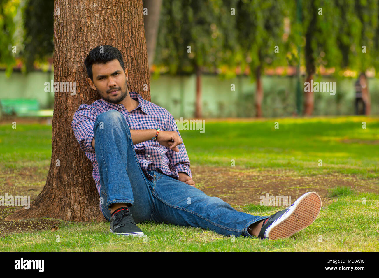 Élégant jeune homme heureux assis sur l'herbe leaning against tree Banque D'Images