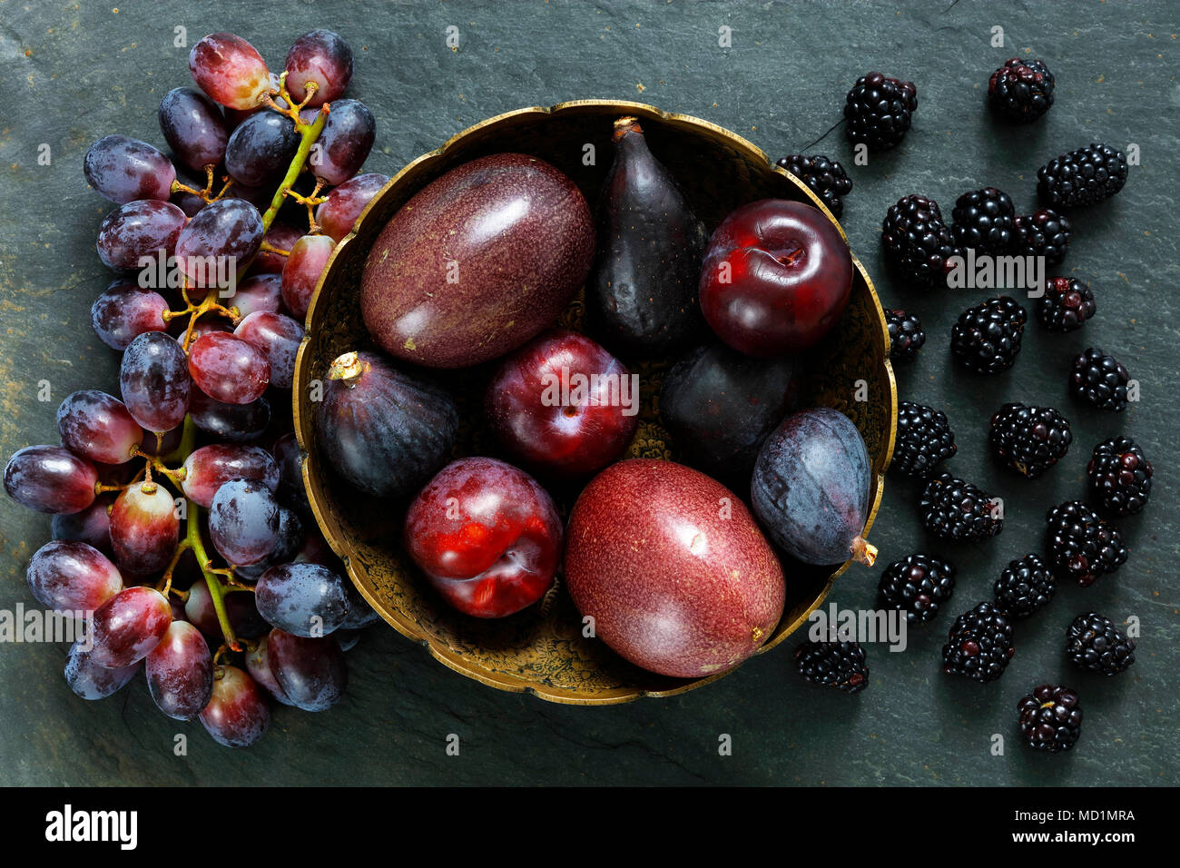 Fruits Exotiques sombre sur fond d'ardoise dont les fruits de la passion, prunes, figues, raisins, de petits fruits noirs Banque D'Images