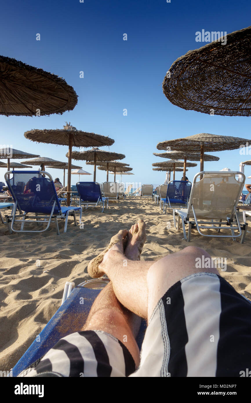 La section basse de barefoot man relaxing on lounge chair plage de sable Banque D'Images