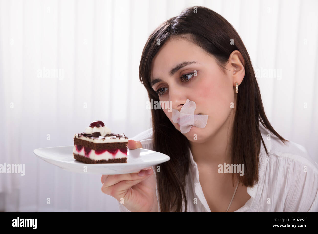 Jeune femme avec du ruban gommé sur la bouche Holding tranche de gâteau sur la plaque Banque D'Images