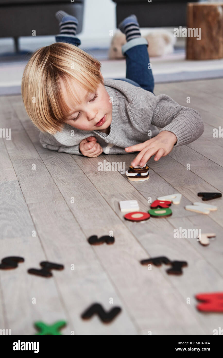 Jeune garçon couché sur le plancher, l'empilement des lettres magnétiques Banque D'Images