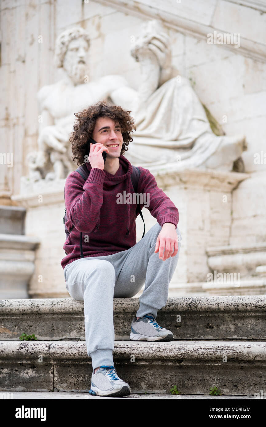 Beau jeune homme avec les cheveux bouclés tracksuit parle sur son téléphone mobile en face de Dieu du Nil statue à Rome Banque D'Images