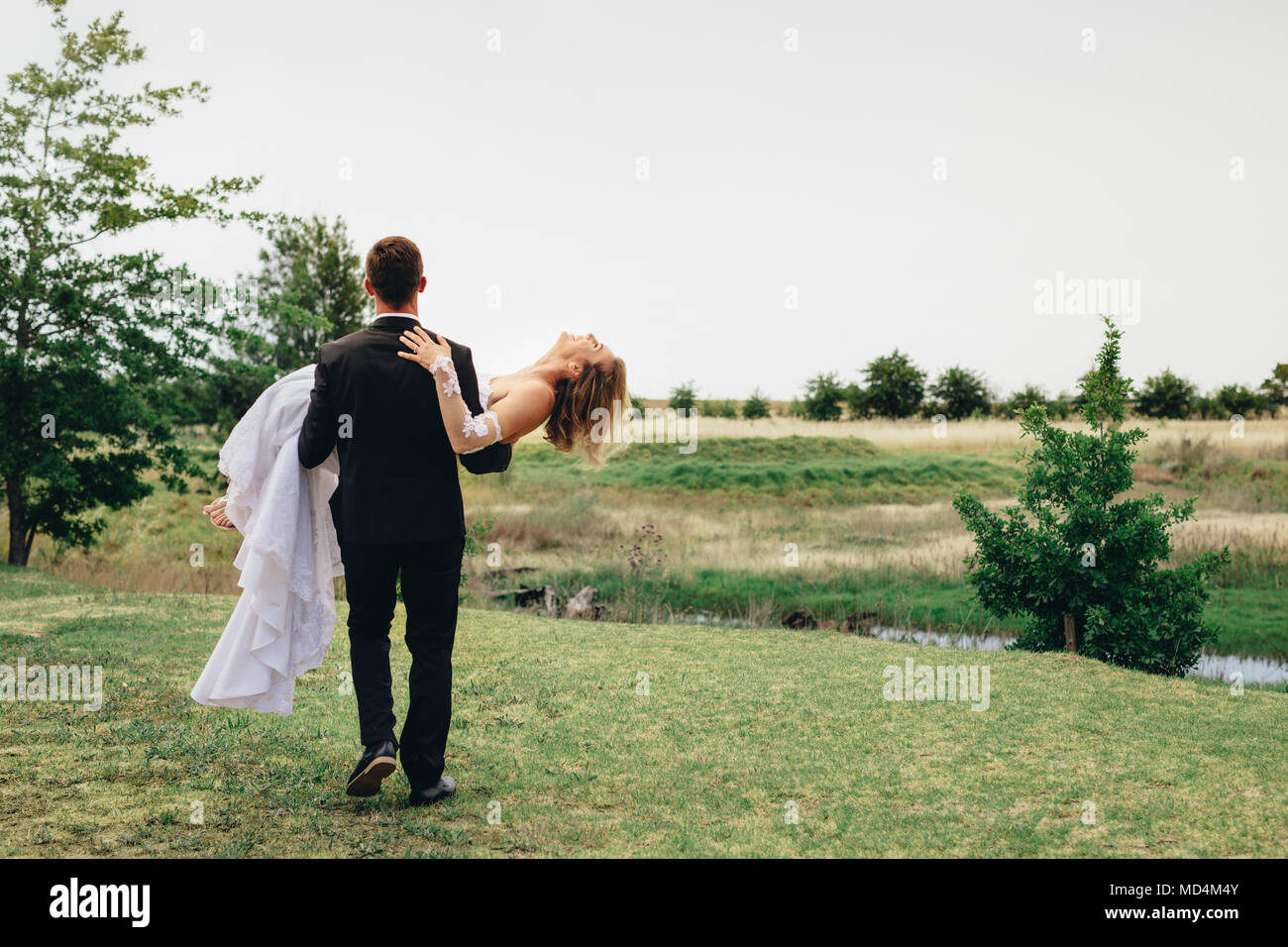 Vue arrière de l'époux avec son épouse et de s'éloigner dans le parc. Newlywed couple célébrant le mariage en plein air. Banque D'Images Vue arrière de l'époux avec son épouse et de s'éloigner dans le parc. Newlywed couple célébrant le mariage en plein air. Banque D'Images