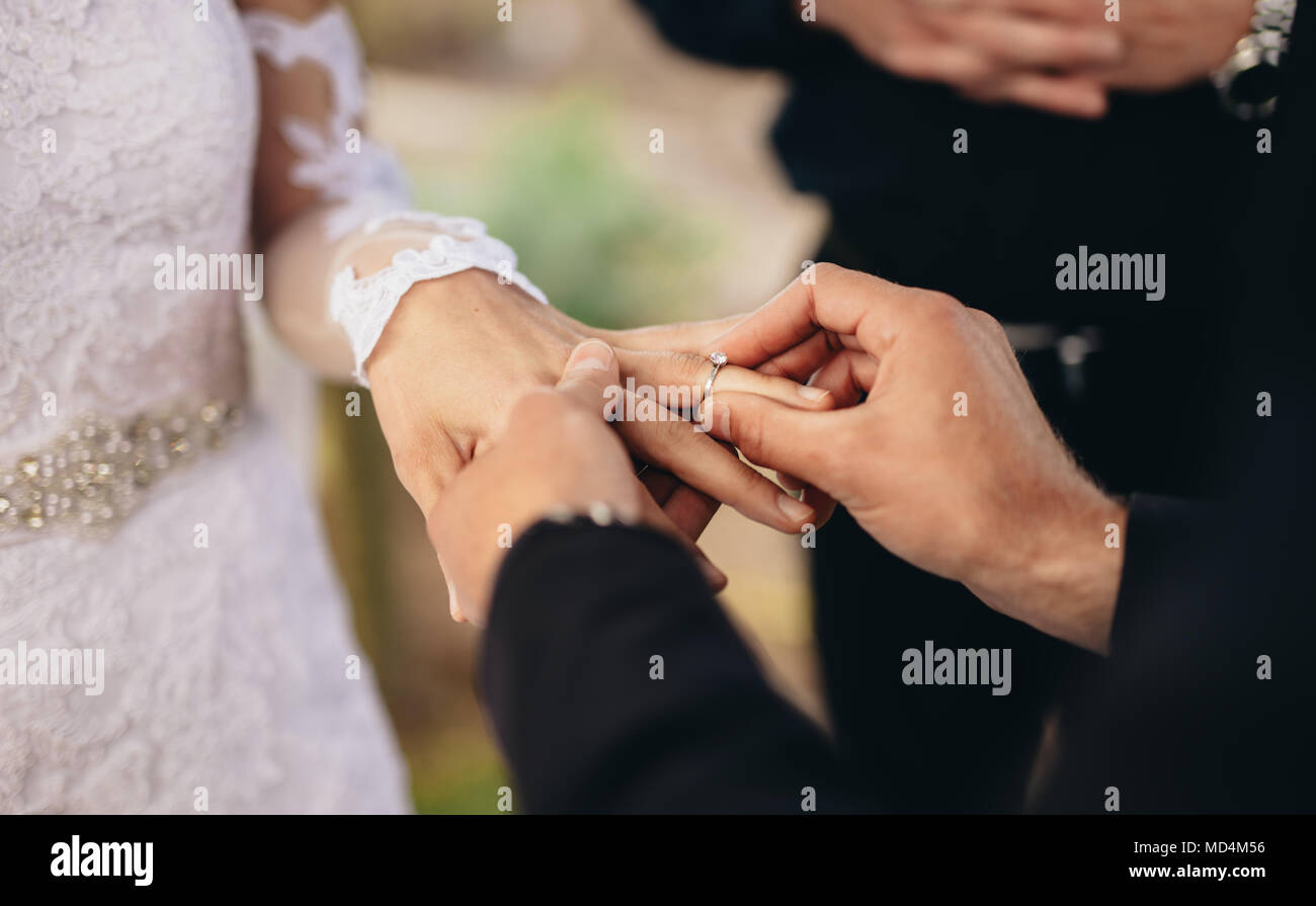 Gros plan du groom de placer un anneau de mariage par correspondance sur la main. Wedding Couple lors d'une cérémonie de mariage en plein air. Banque D'Images Gros plan du groom de placer un anneau de mariage par correspondance sur la main. Wedding Couple lors d'une cérémonie de mariage en plein air. Banque D'Images