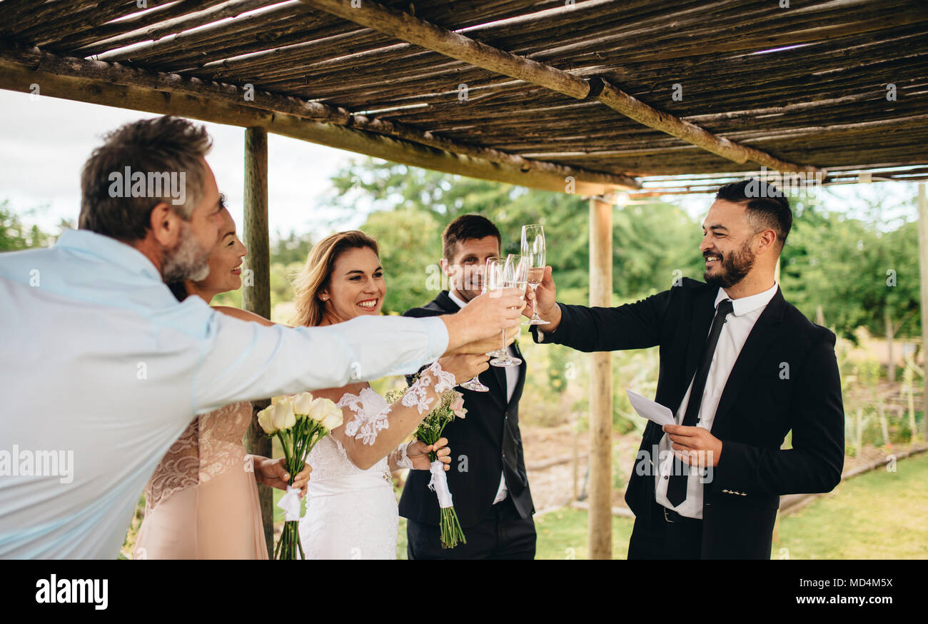 Guest toasting champagne avec couple de mariage. Les jeunes mariés clinking glasses et profiter de l'instant avec l'invité à réception de mariage à l'extérieur. Banque D'Images Guest toasting champagne avec couple de mariage. Les jeunes mariés clinking glasses et profiter de l'instant avec l'invité à réception de mariage à l'extérieur. Banque D'Images