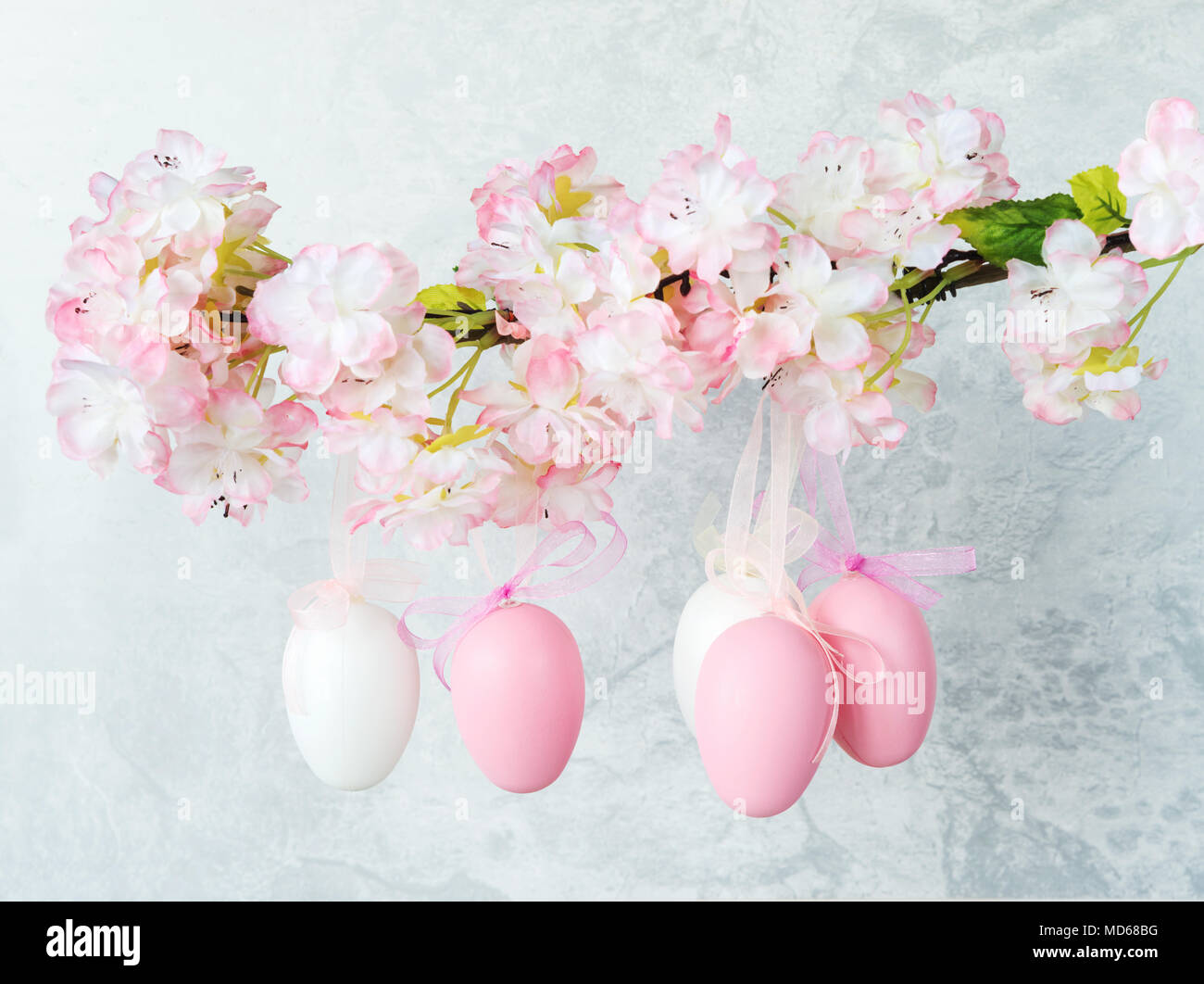 Les oeufs de Pâques blanc et rose, décorée avec des arcs, s'accrocher sur une branche de pommier à fleurs contre un mur de pierre grise Banque D'Images