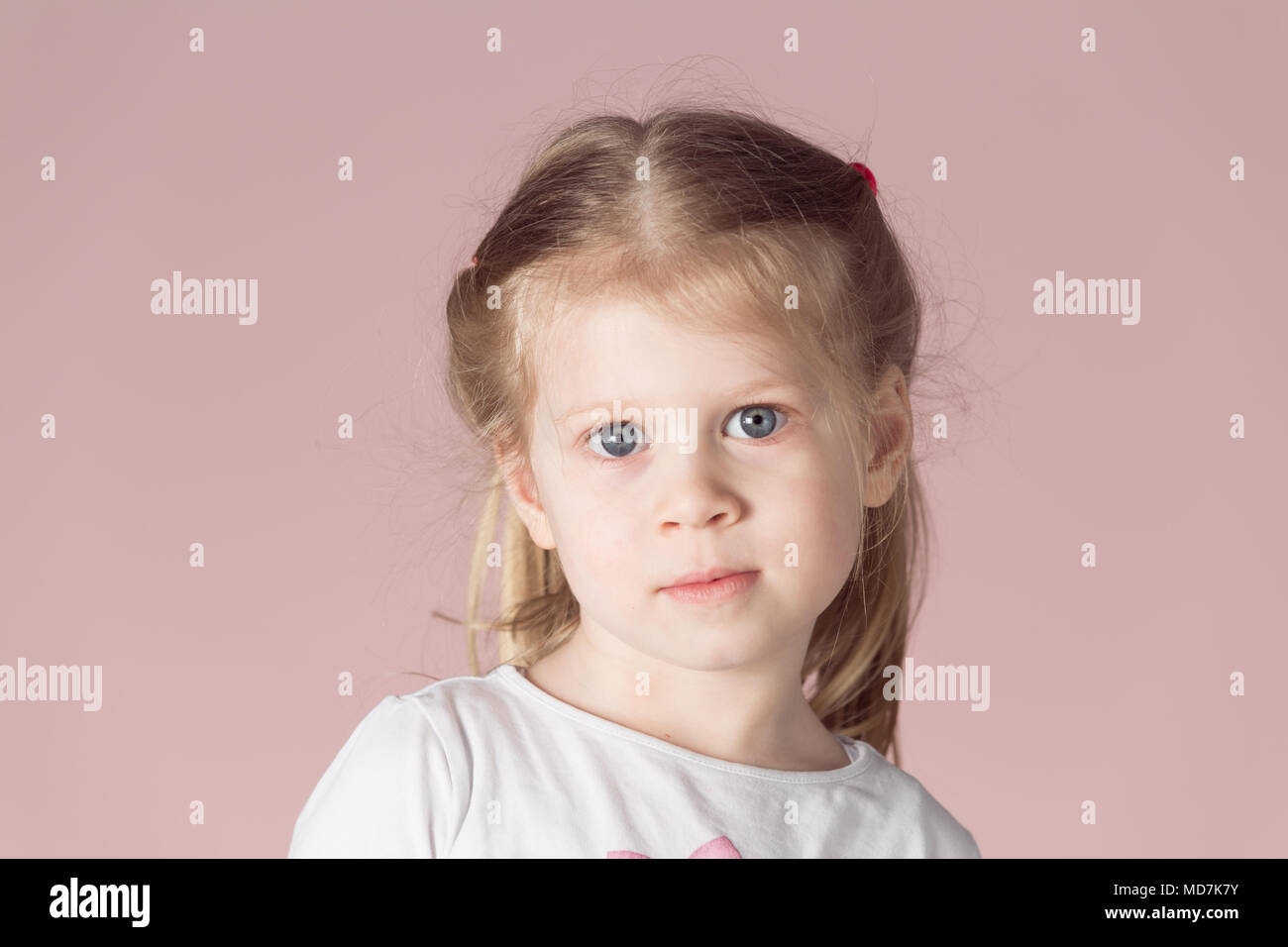 Caucasian girl blonde avec des cheveux ébouriffés. Portrait de petite fille sur fond rose. Banque D'Images
