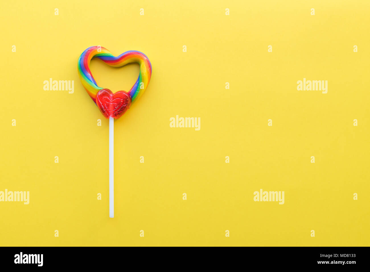 Arc-en-ciel en forme de coeur lollipop swirl sur fond uni jaune vif Banque D'Images