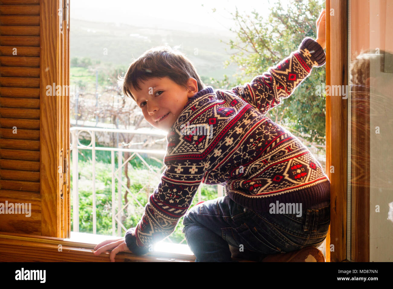 Boy looking at camera, assis sur la fenêtre, Grèce Banque D'Images