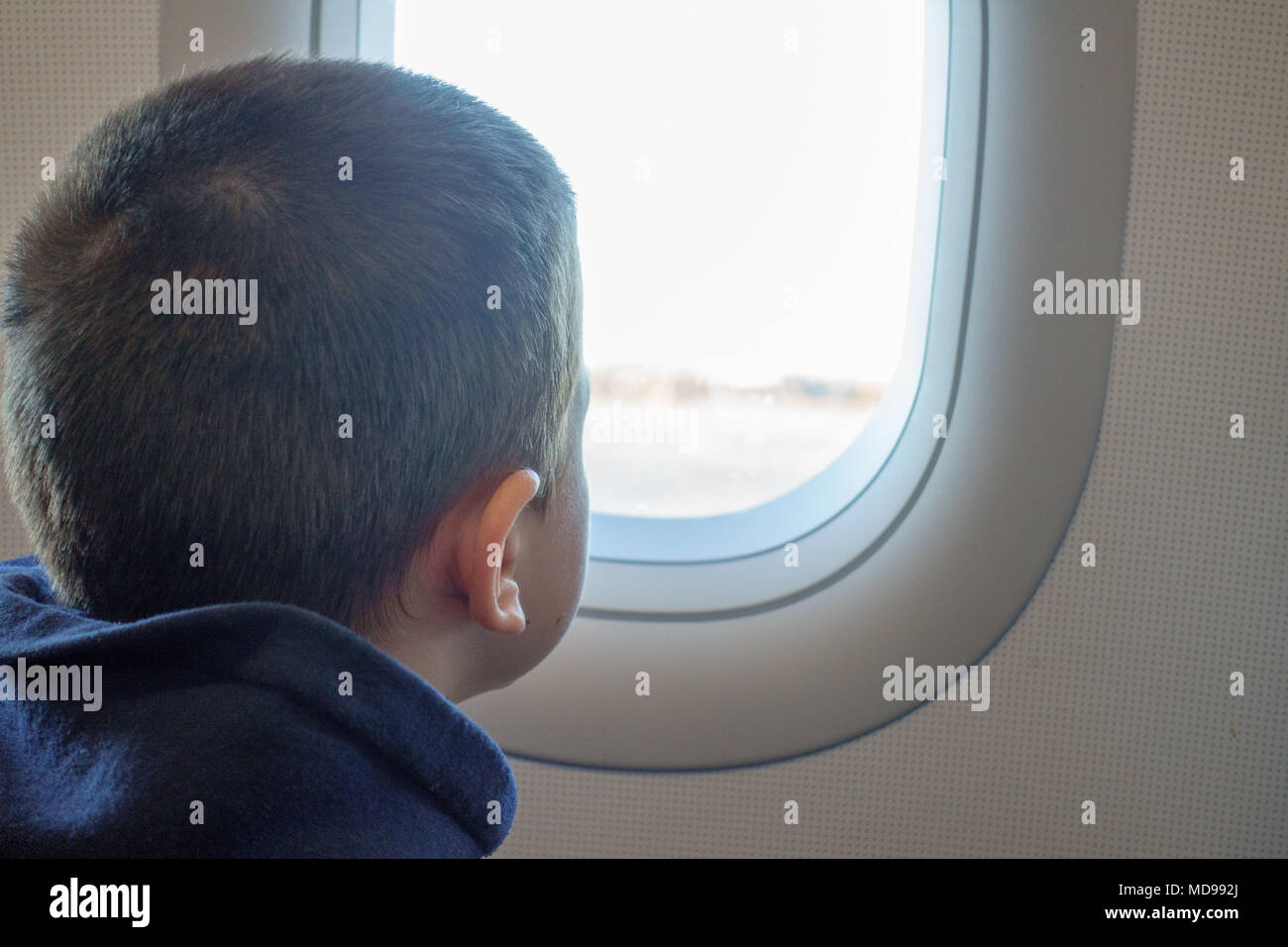 Curieux petit garçon regardant ciel à travers la fenêtre de l'avion Banque D'Images