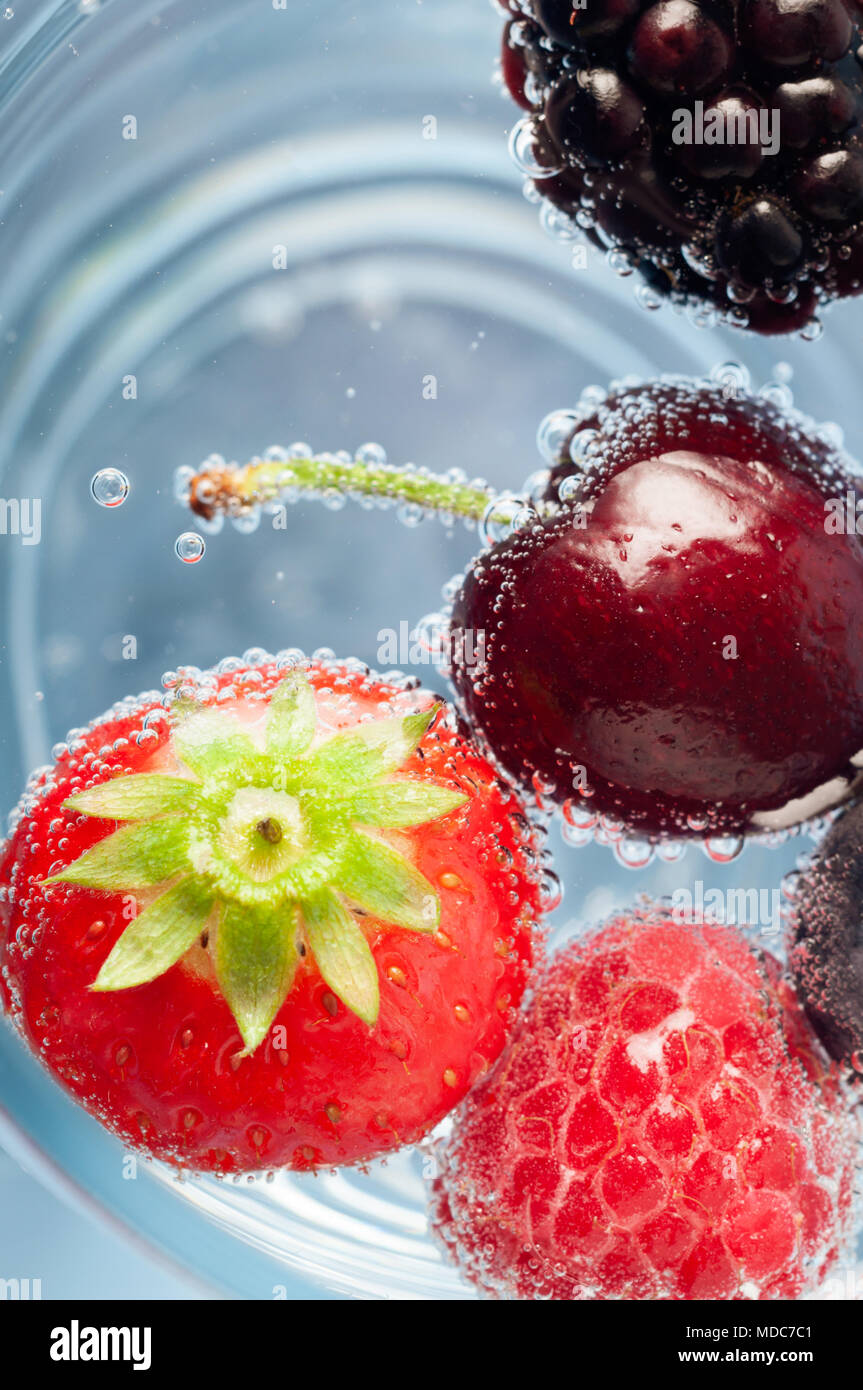Passage près d'une sélection de fruits frais, flottant au-dessus de bleu de l'eau pétillante. Comprend la fraise, cerise, framboise et mûre. Banque D'Images