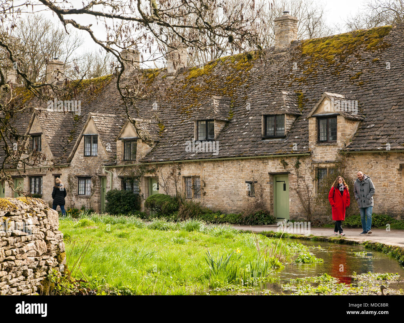 Homme et femme marchant le long de la rivière Coln à l'extérieur de la rangée d'Arlington dans le village anglais Cotswold de Bibury Gloucestershire appartenant au National Trust Banque D'Images
