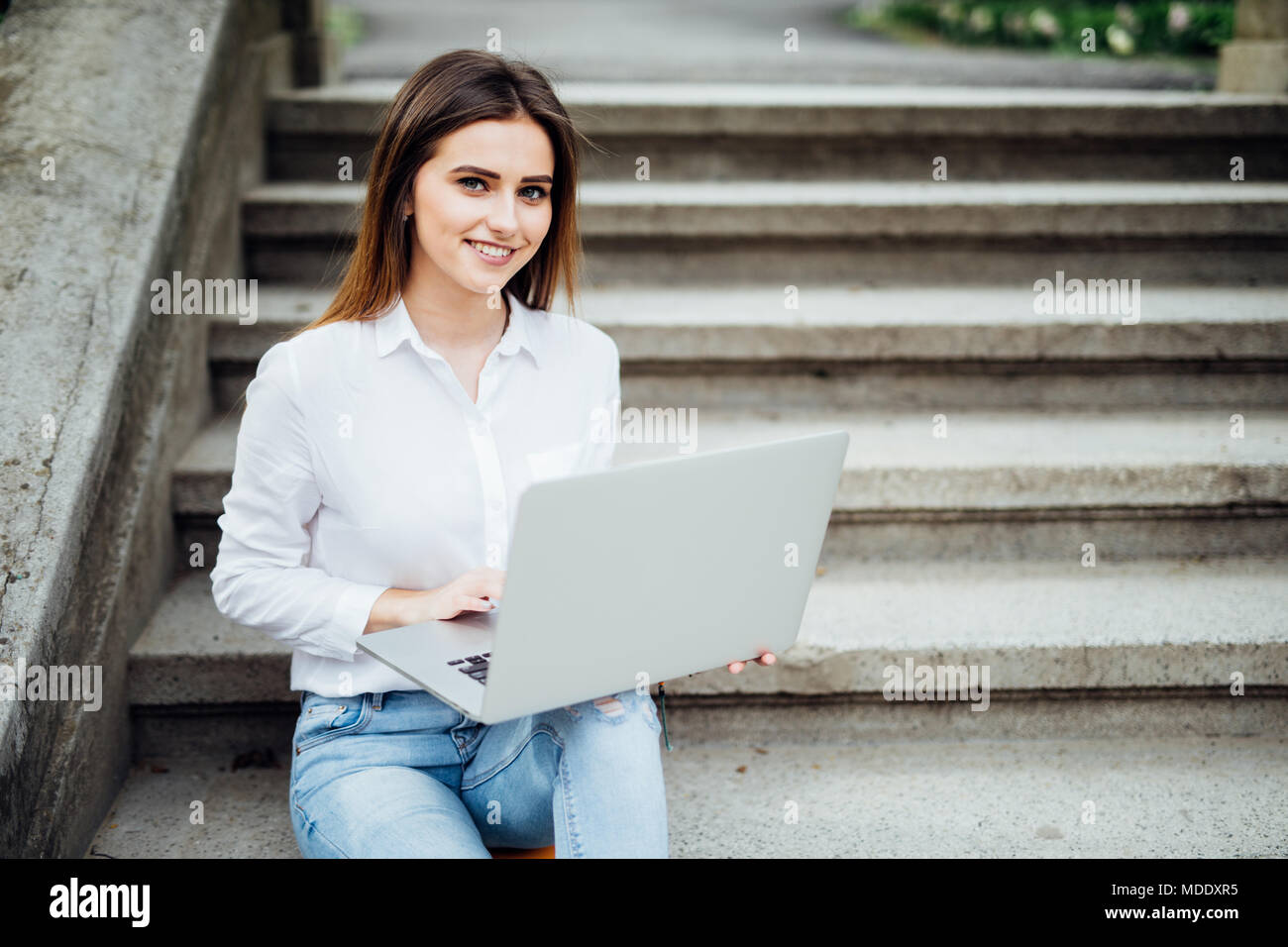 Smiling student girl sitting on stairs travaillant avec un ordinateur portable, la préparation pour les examens à l'extérieur, avoir reste en campus universitaire. Banque D'Images