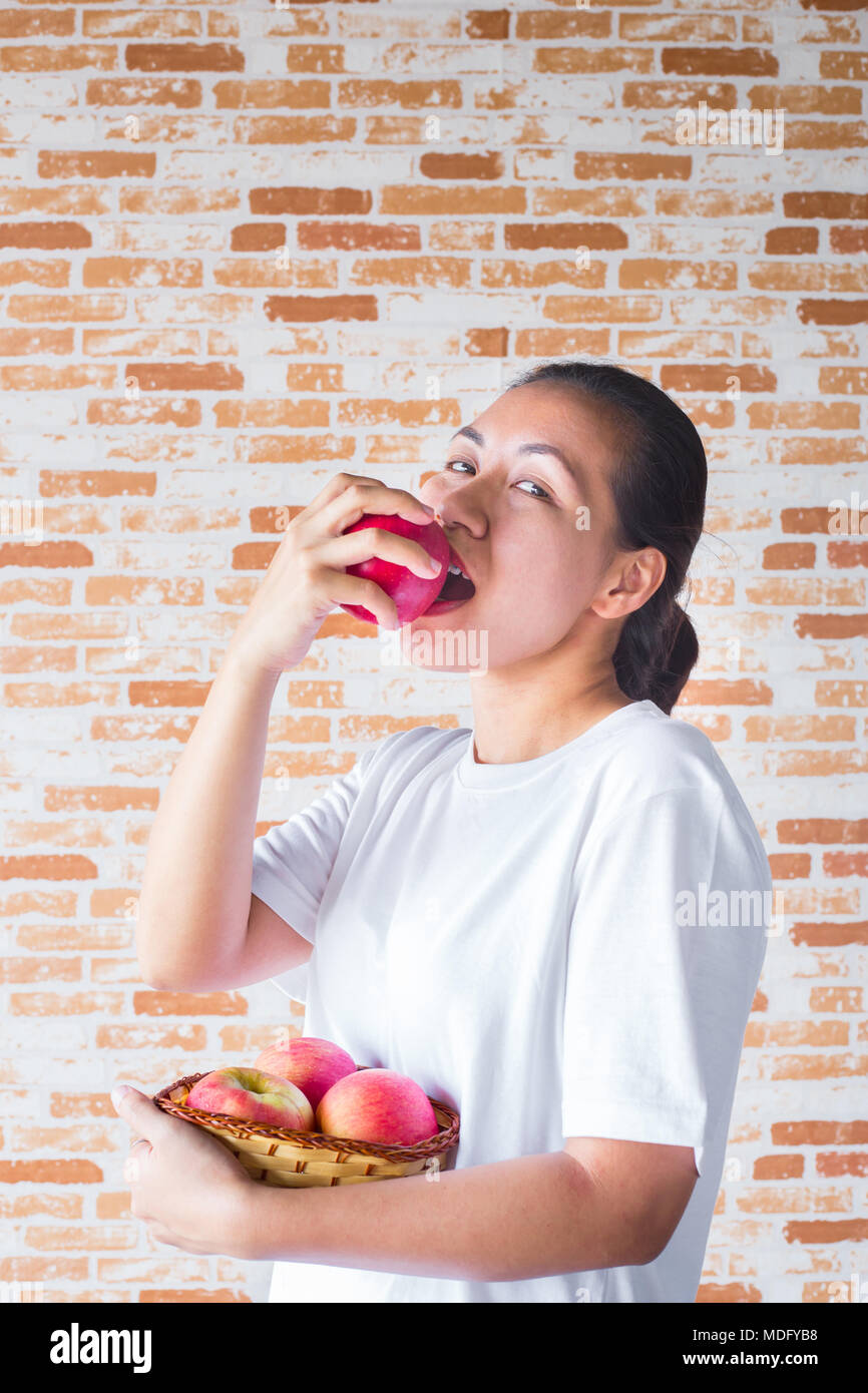 Jeune femme asiatique bouchée de pomme rouge et holding basket aux pommes Banque D'Images