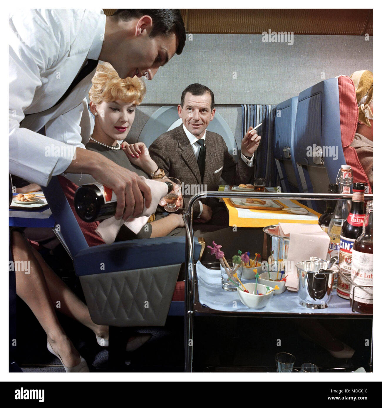 1950s cabine d'avion de première classe de service d'avion de steward servant les passagers de première classe dans les années 1950-1960 Voyage aérien de première classe l'ère d'or de l'aviation de passagers les passagers mâles fumeurs de cigarettes Banque D'Images