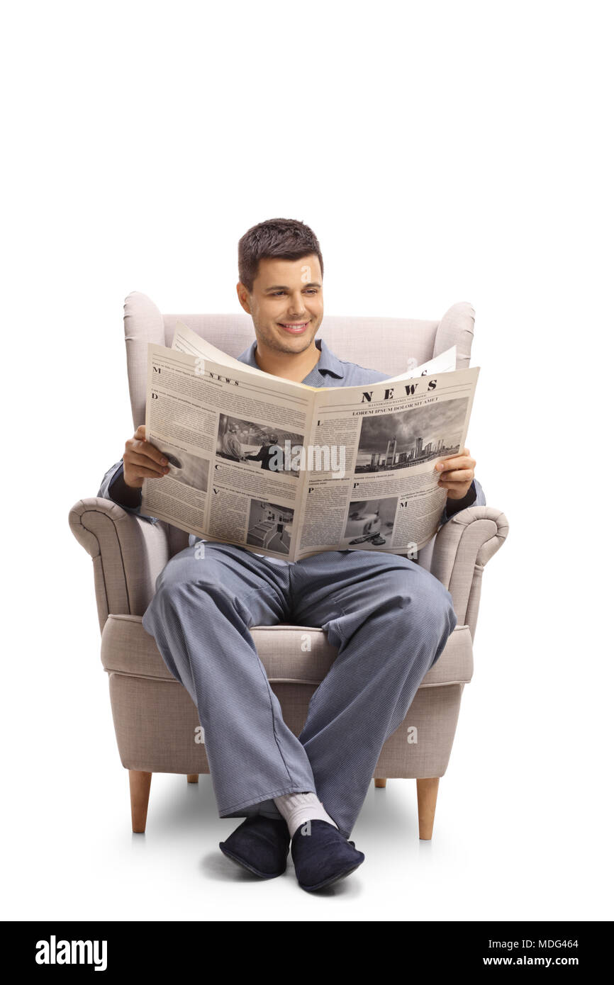 Jeune mec en pyjama assis dans un fauteuil et lit un journal isolé sur fond blanc Banque D'Images