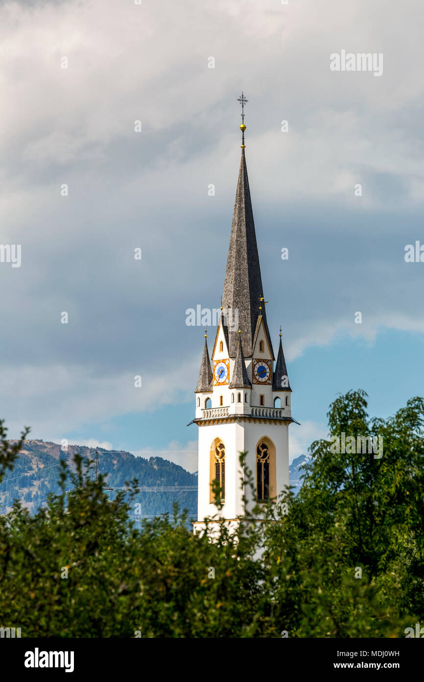 Tour de l'horloge de l'église élaborée avec des arbres en premier plan et nuages sombres à l'arrière-plan, Lienz, Tyrol, Autriche Banque D'Images