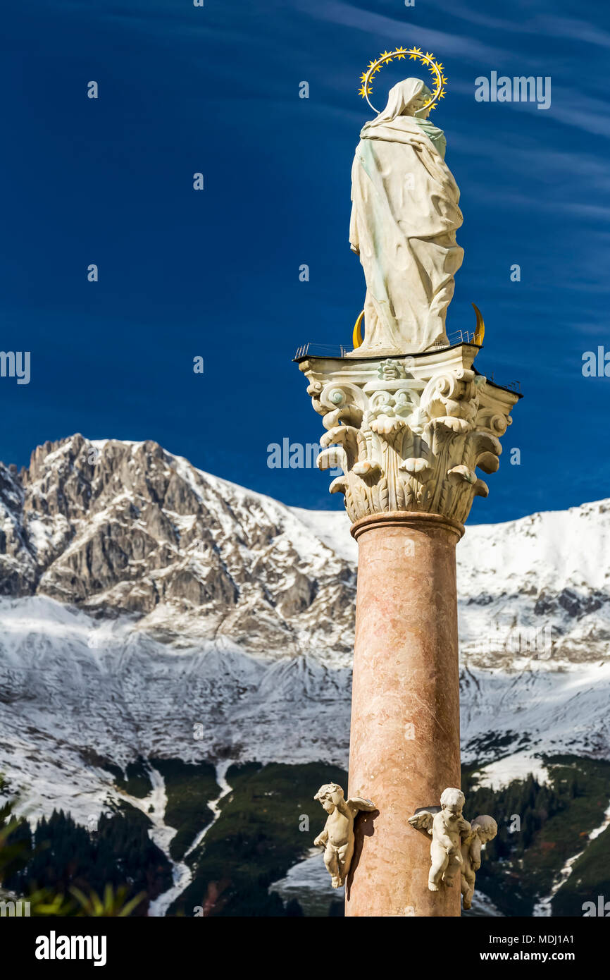 Statue de pierre avec halo en haut de colonne à l'aide d'une chaîne de montagnes couvertes de neige et ciel bleu en arrière-plan, Innsbruck, Tyrol, Autriche Banque D'Images